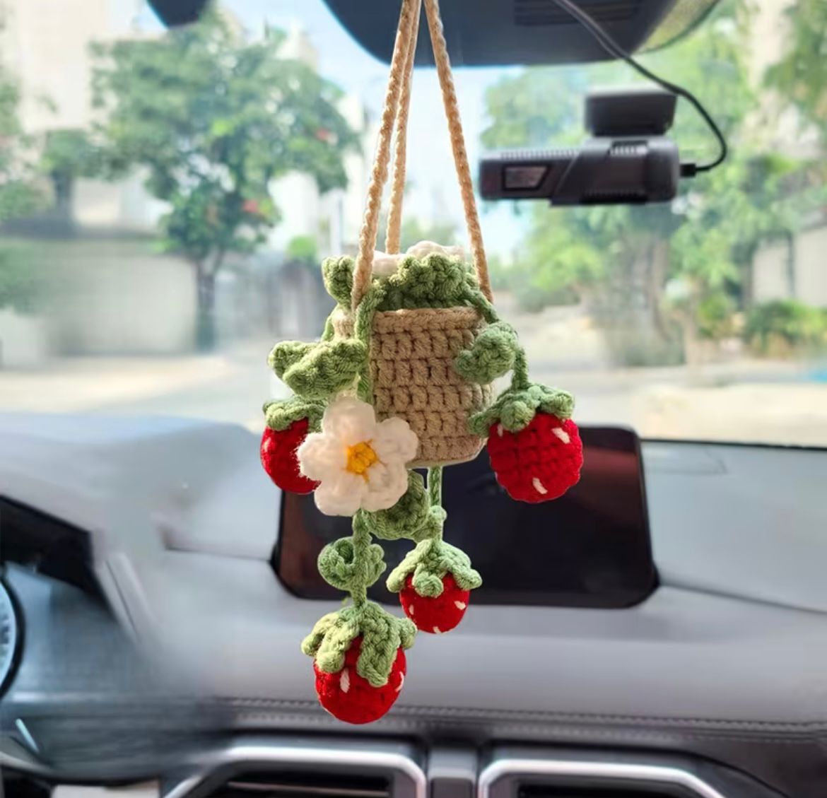 A cute Kashmiri handmade crochet hanging basket with red strawberries and a white flower, hanging on a car mirror.