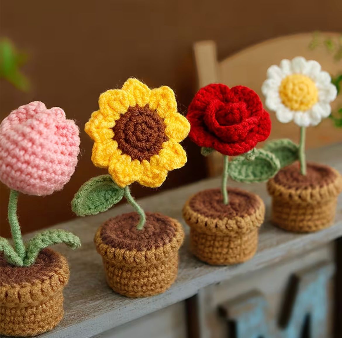 A row of four Kashmiri handmade crochet flower pots including Tulip, Sunflower, Rose, and Daisy on a wooden shelf.